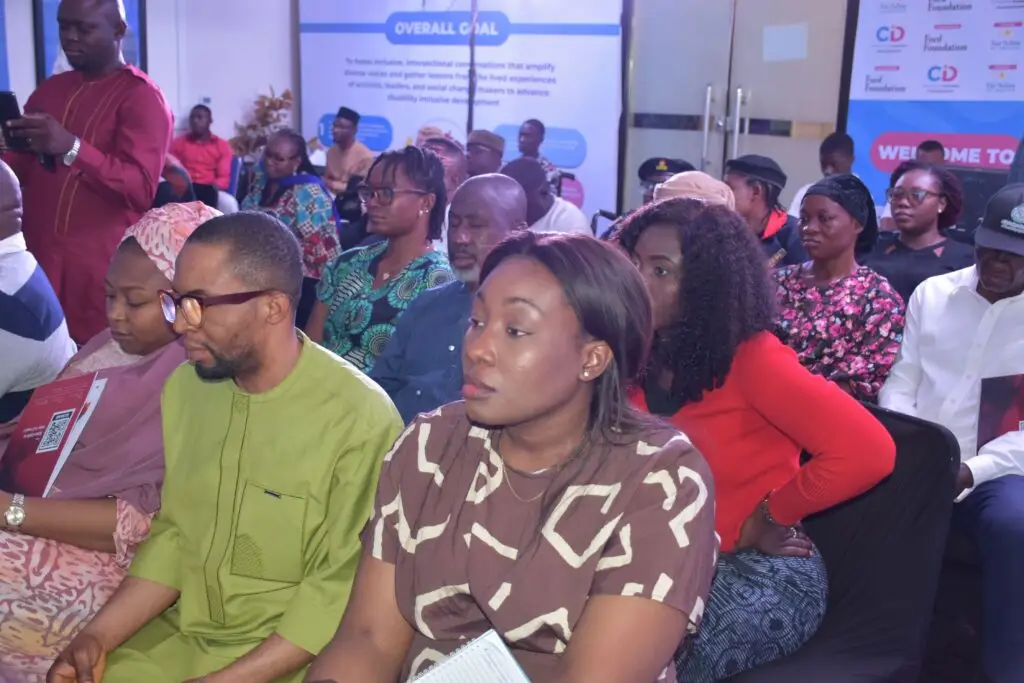 Participants seated in a conference room listening to a presentation during a disability inclusion event organised by the Centre for Inclusive Development (CID). Event banners and information displays are visible in the background while attendees engage with the session