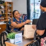 Nigerian woman with a disability running her business and serving a customer in an accessible shop